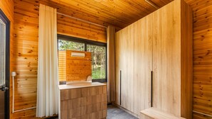 Habitación pequeña con paredes de madera, un banco integrado, una ventana con cortinas y un pequeño equipo de aire acondicionado.