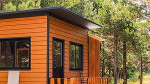 A modern wooden cabin with large windows, a balcony, and a forest backdrop.