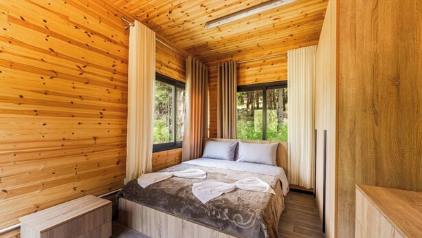 A wooden cabin bedroom with a bed, curtains, and a window.