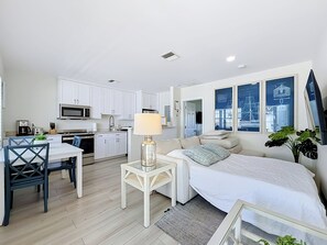 A modern hotel room with a bed, bedside table, and a view of the city through large windows. - COZY CORAL (Lauderdale-by-the-Sea)