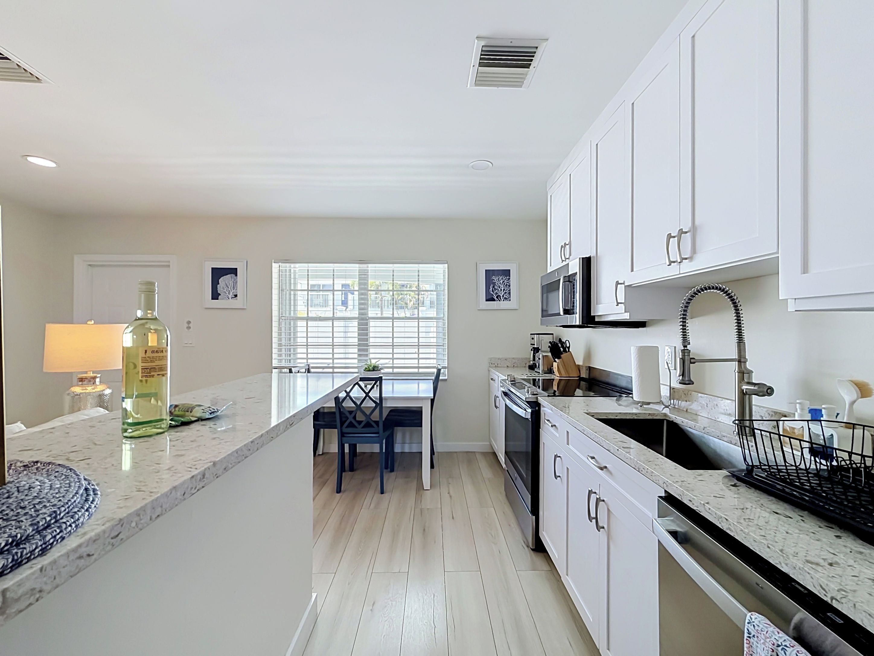 Una cocina moderna con armarios blancos, encimera de mármol y zona de comedor con mesa y sillas.