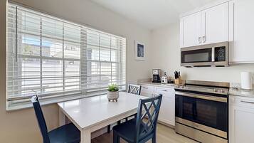 Une cuisine moderne avec des meubles blancs, des appareils en acier inoxydable et un coin repas comprenant une table et des chaises.