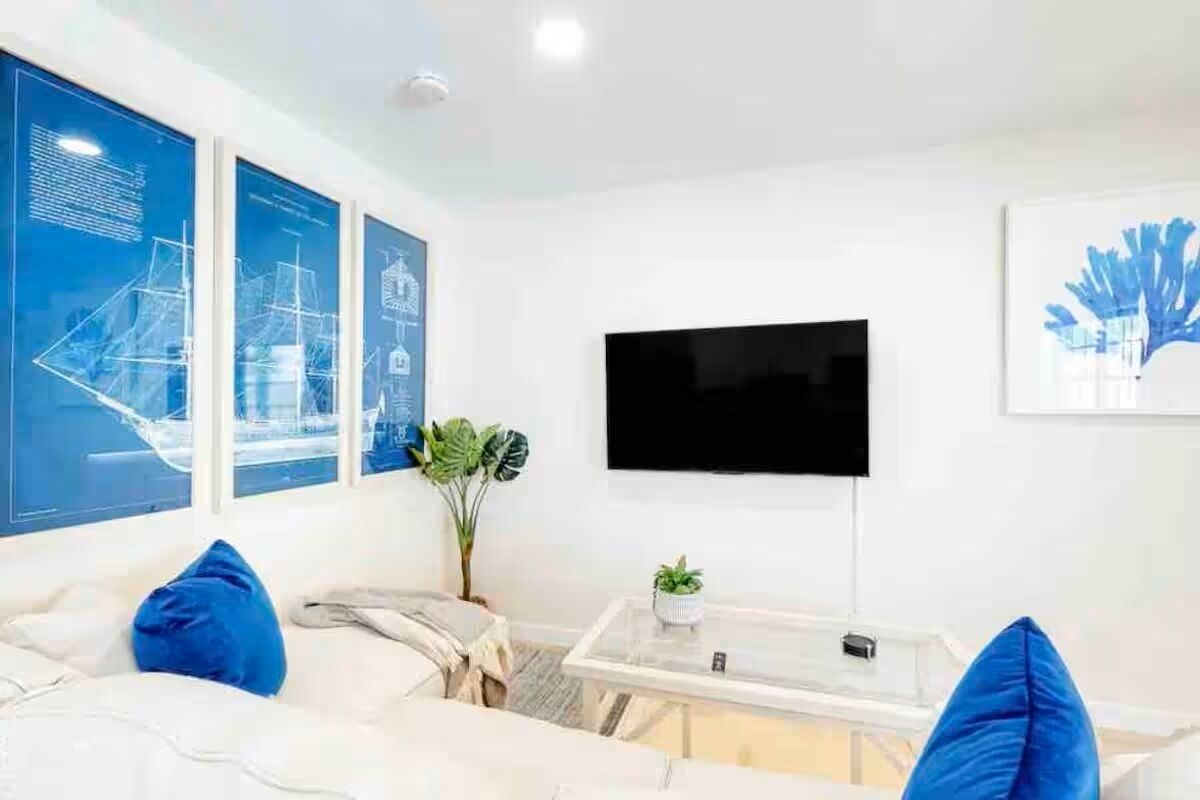 Una sala de estar moderna con un televisor de pantalla plana montado en la pared, un sofá con cojines azules y una mesa de centro con una planta.
