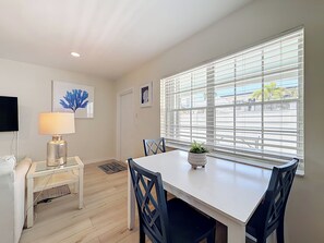 A dining area with a white table, black chairs, a small potted plant, and a lamp on a side table. - COZY CORAL (Lauderdale-by-the-Sea)