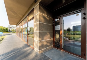 A building entrance with a glass door, a sign indicating room number KL.B, and a covered walkway.
