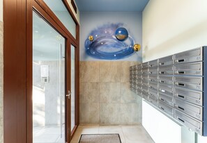 A hallway with a wall-mounted mailbox system and a mural of a space scene. - Tauron Arena Cosy Apartment (Kraków)