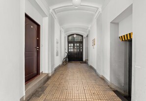 A corridor with a tiled floor, a wooden door, a bicycle, and a black door with a yellow and black stripe. - Kazimierz Riverside Charming Apartment (Kraków)
