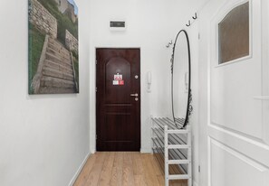 A hallway with a wooden door, a white wall, and a metal rack. - Kazimierz Riverside Charming Apartment (Kraków)