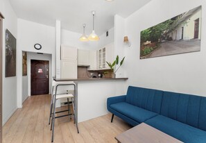 A compact living space with a kitchenette, a blue sofa, a dining table, and a ladder. - Kazimierz Riverside Charming Apartment (Kraków)