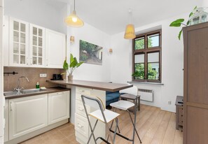 A modern kitchen with white cabinets, a built-in sink, and a window with a view of greenery. - Kazimierz Riverside Charming Apartment (Kraków)
