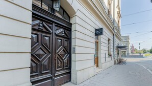 Ein Gebäude mit einer großen, verzierten Holztür, einem gepflasterten Bürgersteig und Blick auf die Straße.