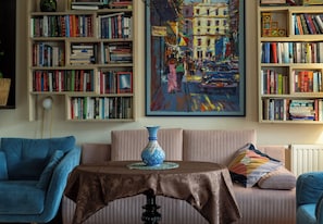 Ein Wohnzimmer mit einem blauen Sofa, einem Tisch mit einer dekorativen Vase und Bücherregalen voller Bücher.