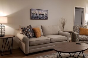 A living room with a sofa, two side tables, a coffee table, and a painting on the wall.