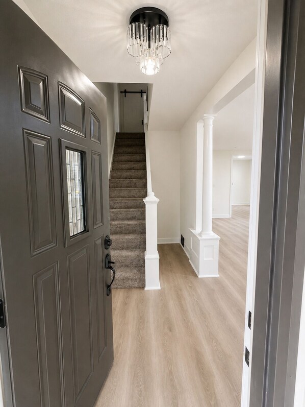 A hallway with a dark door, a staircase, and a chandelier.