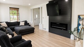 En moderne stue med en hjørnesofa, et fladskærms-tv monteret på en mørk væg og en pejs.