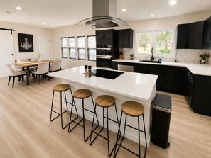 Una cocina moderna con una isla central, taburetes de bar y un comedor con mesa y sillas.