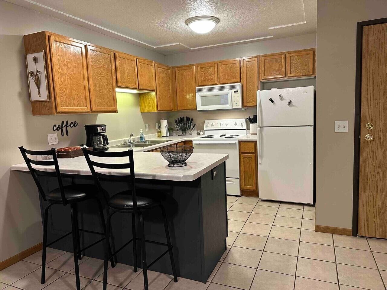 A kitchen with wooden cabinets, a central island with bar stools, a microwave, a stove, and a refrigerator.
