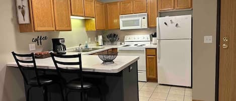 A kitchen with wooden cabinets, a central island with bar stools, a microwave, a stove, and a refrigerator.