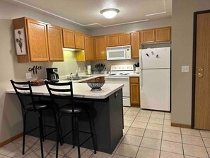 A kitchen with wooden cabinets, a central island with bar stools, a microwave, a stove, and a refrigerator.