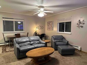 A living room with a ceiling fan, two leather sofas, a coffee table, and a dining area with a table and chairs.