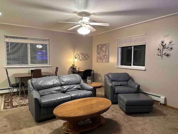 A living room with a ceiling fan, two leather sofas, a coffee table, and a dining area with a table and chairs.