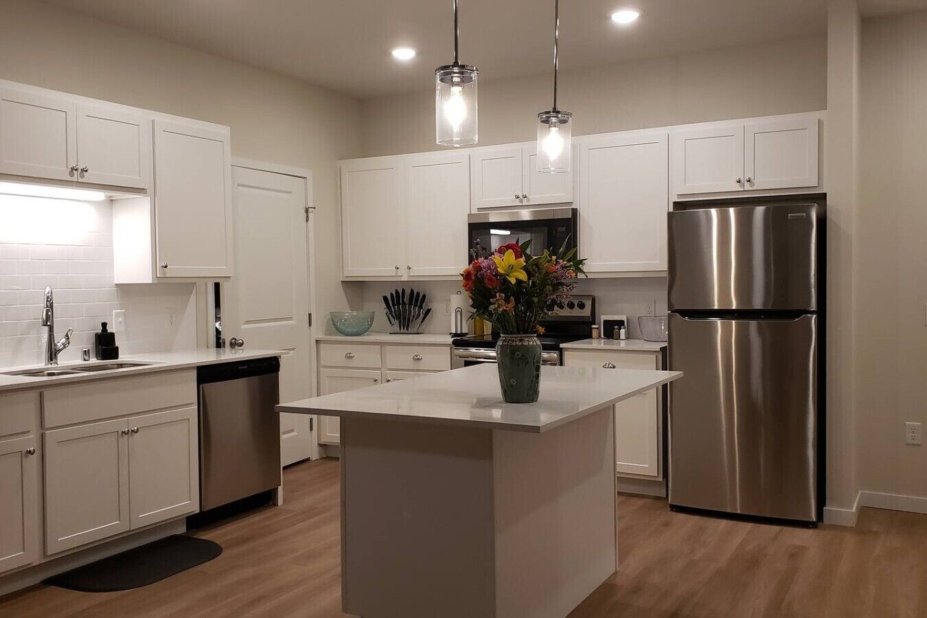 A modern kitchen with white cabinetry, a stainless steel refrigerator, and a central island with a vase of flowers.