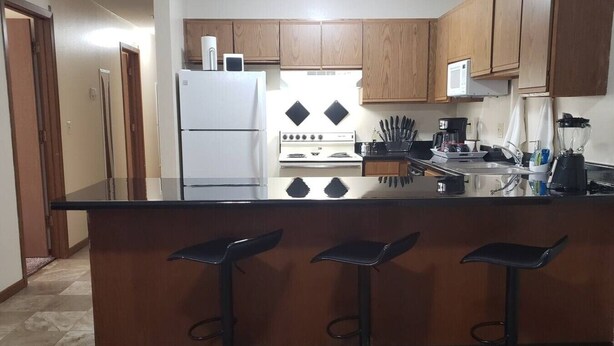 A kitchen with a central island, bar stools, a refrigerator, stove, and various kitchen appliances.