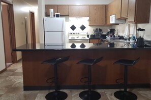 A kitchen with a central island, bar stools, a refrigerator, stove, and various kitchen appliances.