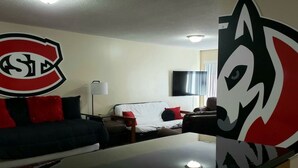 A hotel room with a bed, a sofa, a TV, and a wall with a logo.