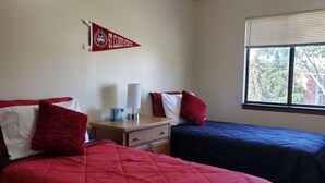 A room with two beds, a nightstand, a lamp, and a window with a view.