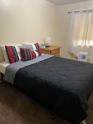 A single bed with a black quilted cover, a wooden nightstand with a lamp, and a white air purifier. - Husky House! Apt for your group 1.5 mi from Campus (St. Cloud)