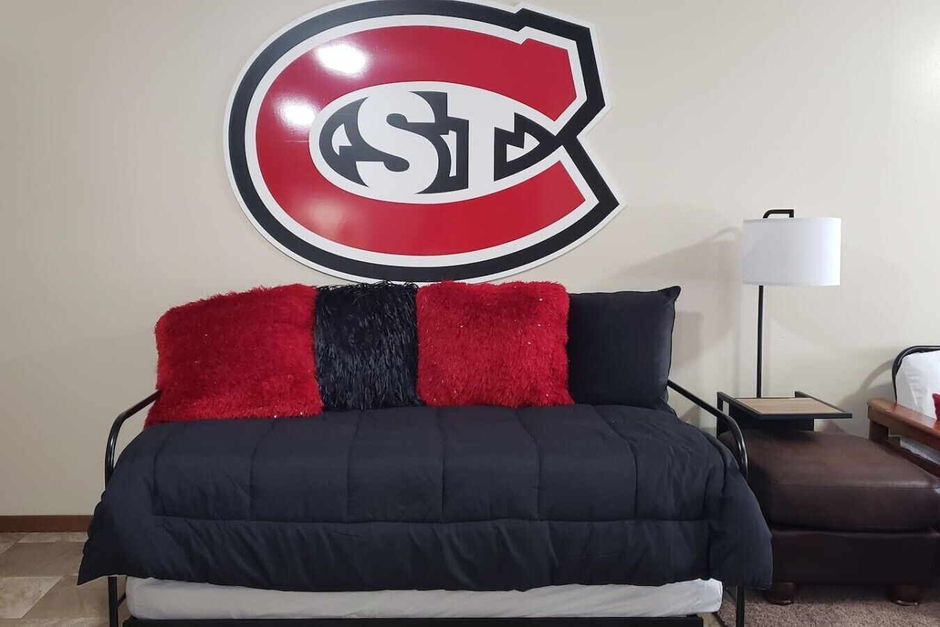 Un lit avec une couverture noire et rouge, un oreiller rouge et noir, et un logo fixé au mur.