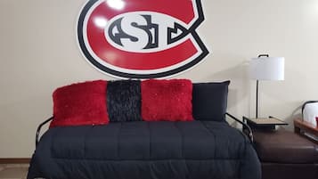 A bed with a black and red blanket, a red and black pillow, and a wall-mounted logo.