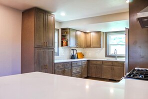 A kitchen with wooden cabinets, a white countertop, and a gas stove. - Historic 4 BR Copper Mine House/ Sauna /Near Trails & Downtown Calumet (Laurium)