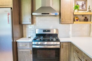 A kitchen with a stainless steel stove, a built-in oven, and wooden cabinets. - Historic 4 BR Copper Mine House/ Sauna /Near Trails & Downtown Calumet (Laurium)