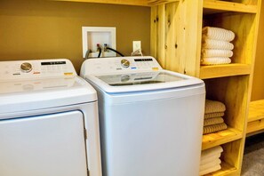 A laundry area with two washing machines and a wooden shelf with folded towels. - Historic 4 BR Copper Mine House/ Sauna /Near Trails & Downtown Calumet (Laurium)
