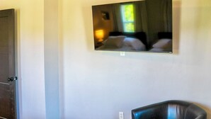 Ein Zimmer mit an der Wand befestigtem Fernseher, einer Tür und einem Stuhl.