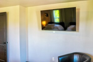 A room with a television mounted on the wall, a door, and a chair. - Historic 4 BR Copper Mine House/ Sauna /Near Trails & Downtown Calumet (Laurium)
