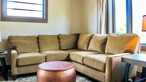 Ein Eckwohnzimmer mit einem beigefarbenen Ecksofa, einem runden Couchtisch aus Kupfer und einem kleinen Beistelltisch.