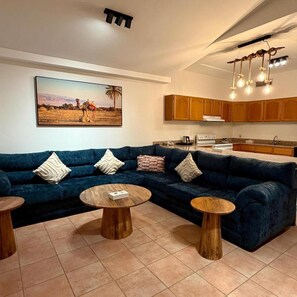 Una sala de estar con un sofá azul oscuro, dos mesas de centro de madera y un cuadro con paisaje desértico.