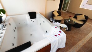 Une salle de bain moderne dotée d’une grande baignoire, d’une douche à parois de verre et d’un coin salon avec deux fauteuils et une petite table.