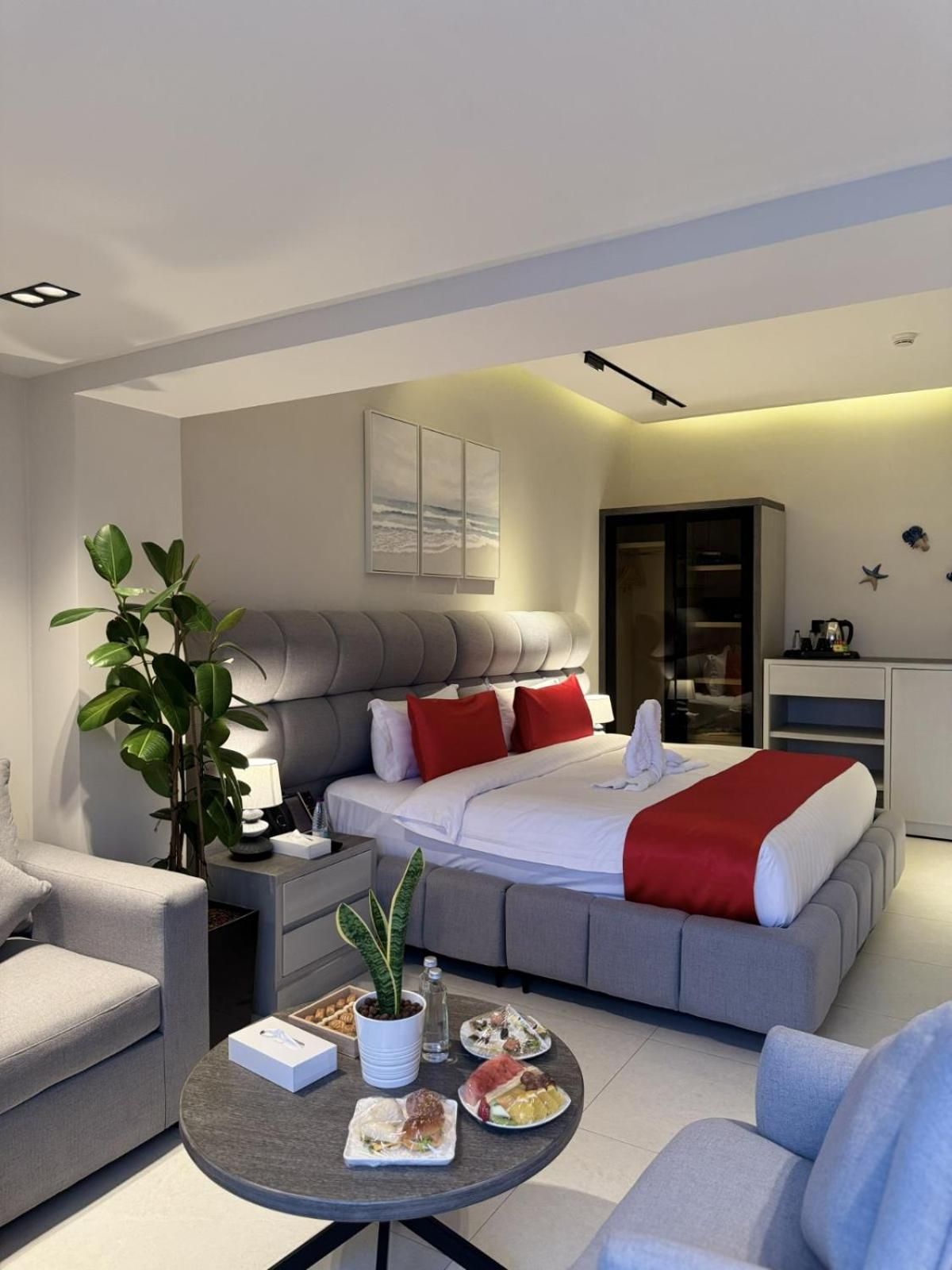 A modern hotel room with a large bed, a seating area with a coffee table, and a plant.
