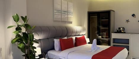 A modern hotel room with a large bed, a seating area with a coffee table, and a plant.