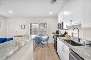 A modern kitchen with white cabinets, a granite countertop, and a built-in oven. - THE SEA MIST (Lauderdale-by-the-Sea)