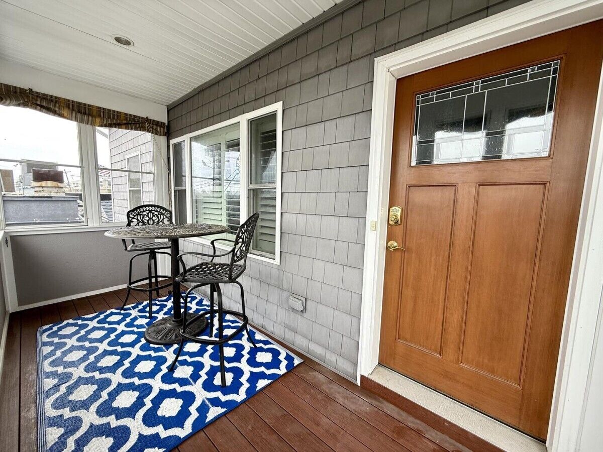 A covered porch with a table and chairs, a wooden door, and a patterned rug.