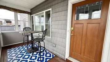 A covered porch with a table and chairs, a wooden door, and a patterned rug.