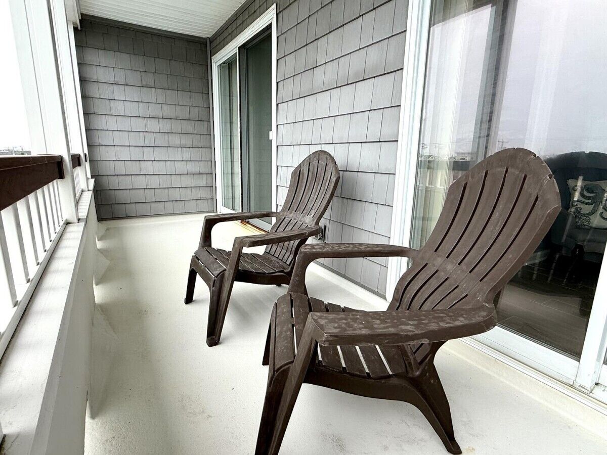 Two Adirondack chairs on a porch with a white railing and a gray siding wall.