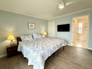 Une chambre à coucher comprenant un lit, deux tables de chevet avec des lampes, un téléviseur à écran plat fixé au mur et une porte donnant accès à une salle de bain.