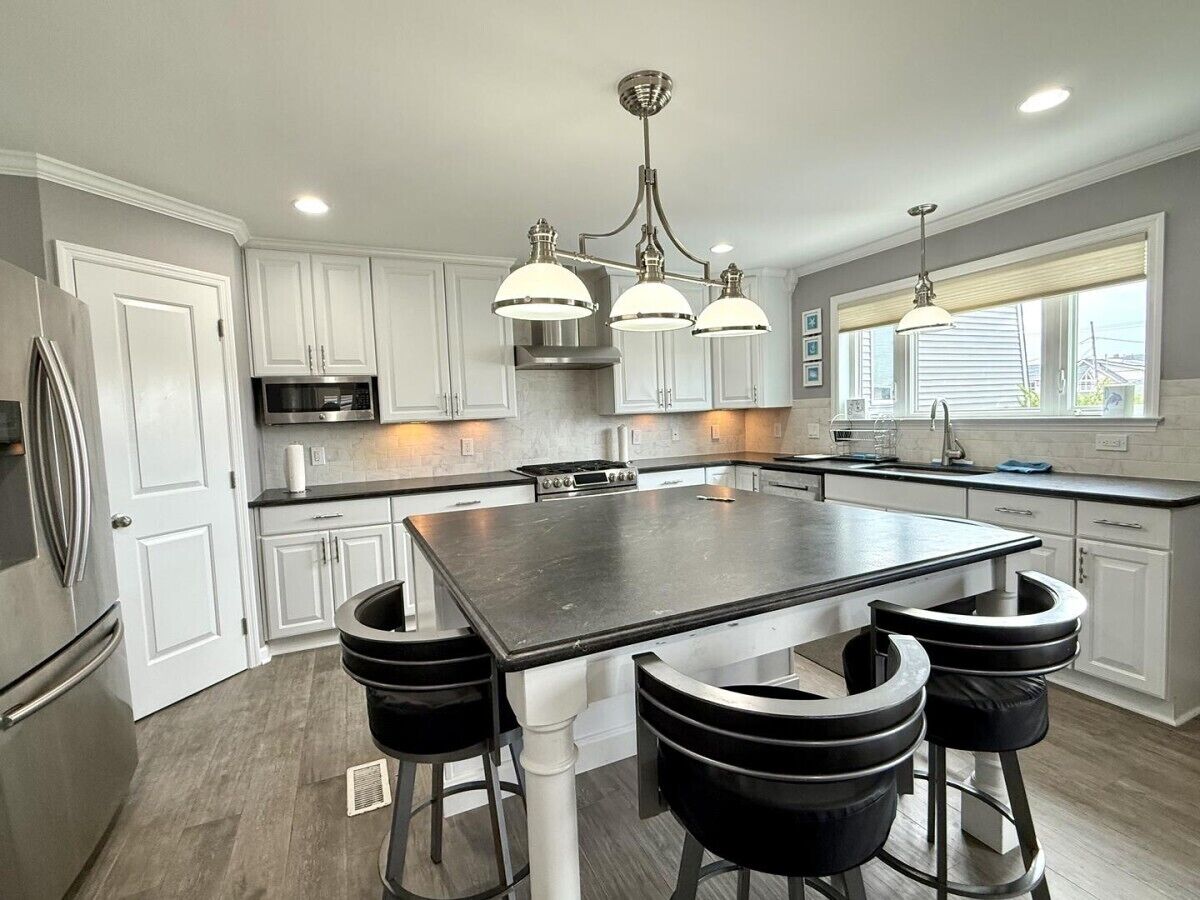 A modern kitchen with a large island, white cabinetry, stainless steel appliances, and pendant lighting.