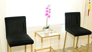 Two black chairs with a clear glass table between them, a potted orchid on the table, and a white curtain in the background. - Wynter Luxe  (Peachtree City)